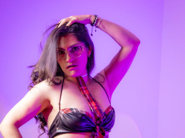 RapZelly with glasses, long brown hair, plaid necktie, black leather bra, raising arm, purple and pink lighting, bracelet, looking serious, showing her tits.