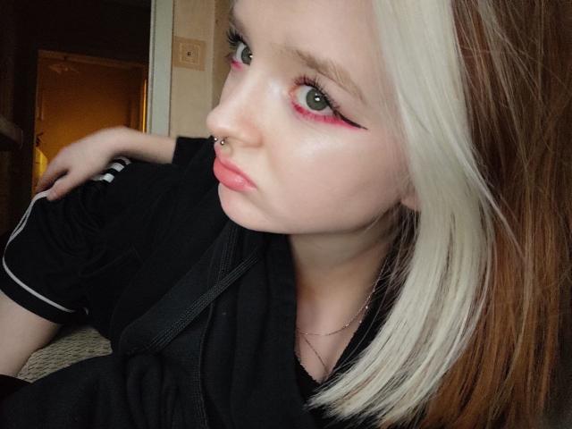 LaPochka with pale skin, green eyes, pink eyeliner, nose ring, and white-brown hair. Wearing black shirt, pouting lips, looking at camera. Boobs partially visible.