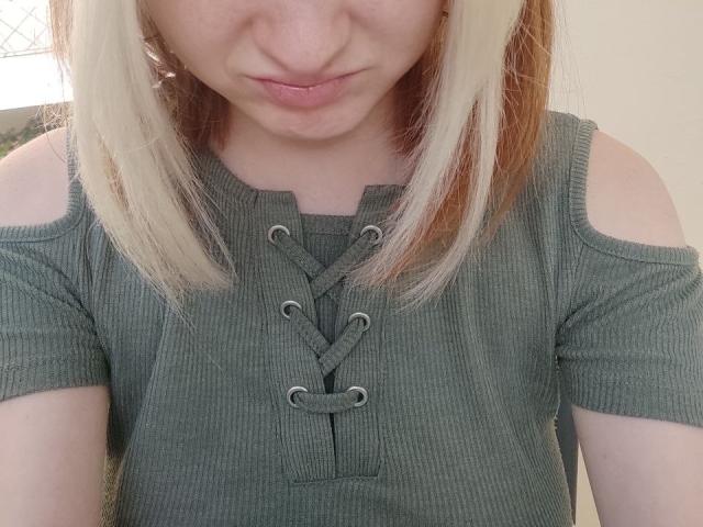 LaPochka, con capelli biondi e castani, indossa una maglietta verde a coste con spalle scoperte e allacciatura frontale, con un'espressione leggermente accigliata, che guarda in basso. Una maglietta orribile, ma è in qualche modo carina..