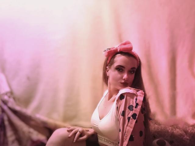 KariMillie mit rosa Stirnband mit Punkten, weißem Sport-BH und rosa Jacke, Hände im Haar, rosa Beleuchtung, weicher Fokus, Halbnahaufnahme, zeigt Brüste, süß, selbstbewusster Ausdruck..