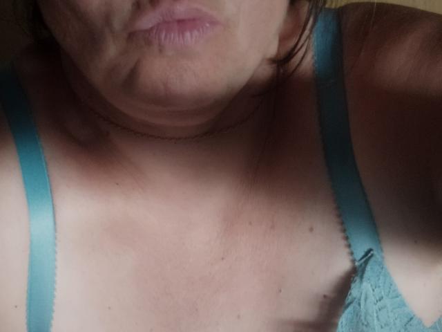 La parte superior del pecho de Aline69, mostrando piel pálida y tirantes de encaje azul, con labios ligeramente fruncidos y un rostro sombreado. Los senos son parcialmente visibles..