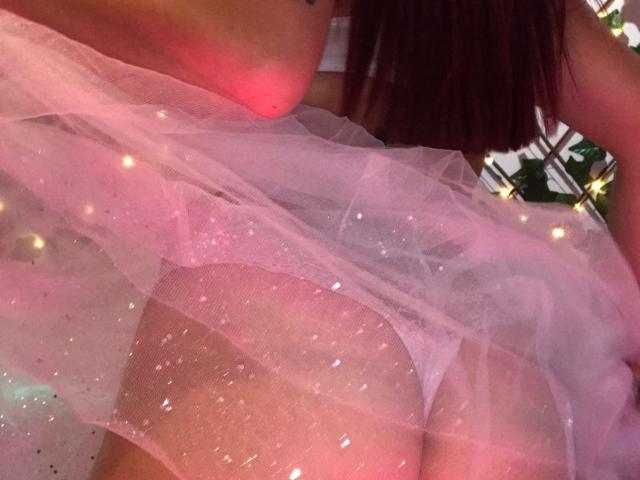 Het achterwerk van Camila Coleman, te zien in roze, glinsterende, doorschijnende onderbroeken, zichtbaar door een verleidelijke, roze, glinsterende rok, met haar rug naar de camera gericht, en haar bruine haar rechtsboven in beeld..