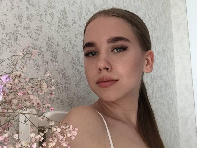 BunnyNiki a un visage mignon avec une peau claire, des yeux bleus et des cheveux bruns attachés en queue de cheval. Elle porte un haut blanc, et il y a une branche de cerisier rose..