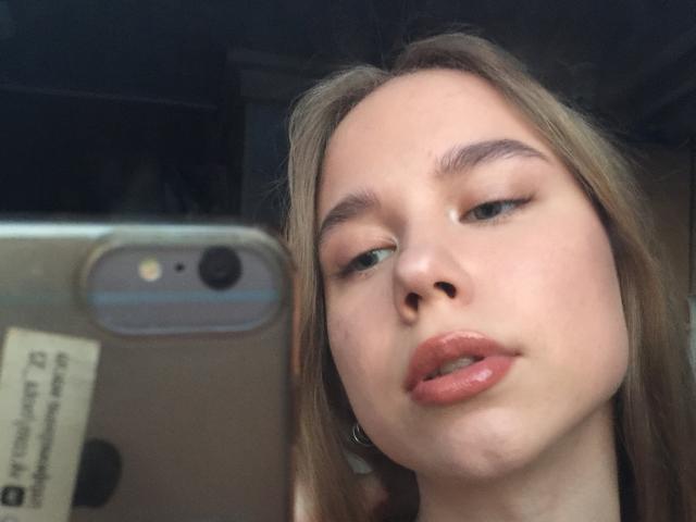 Le visage de BunnyNiki sur une photo, tenant un téléphone avec un appareil photo et un autocollant. Elle a la peau claire, les yeux marron, des lèvres pleines roses, et des lèvres légèrement entrouvertes roses..