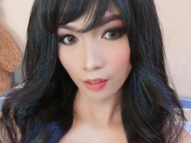 FoxyDreamTs heeft lang zwart haar, groene ogen, roze lippenstift en lichte make-up. Ze kijkt recht in de camera met een lichte, sensuele glimlach. Haar borsten zijn niet zichtbaar..