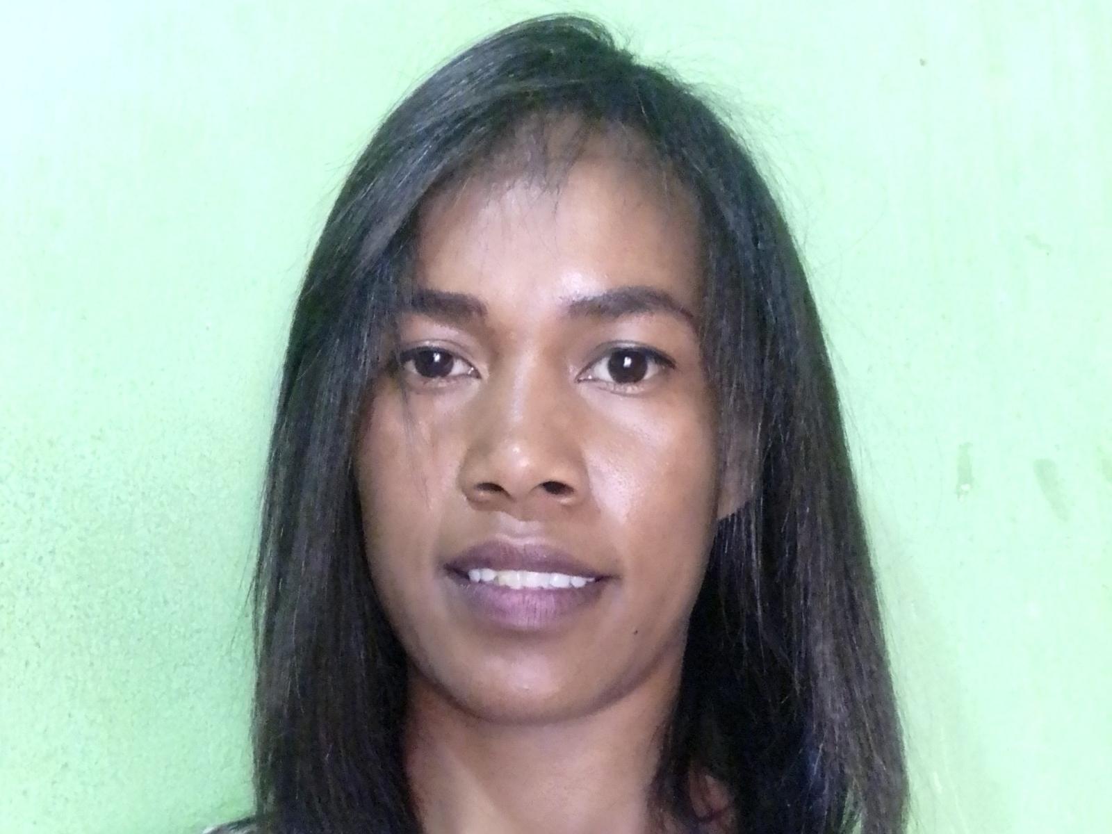 DivanahOh tiene la piel de color marrón oscuro, cabello negro lacio y está sonriendo, mostrando sus dientes. Tiene ojos pequeños y oscuros y lleva una blusa oscura..