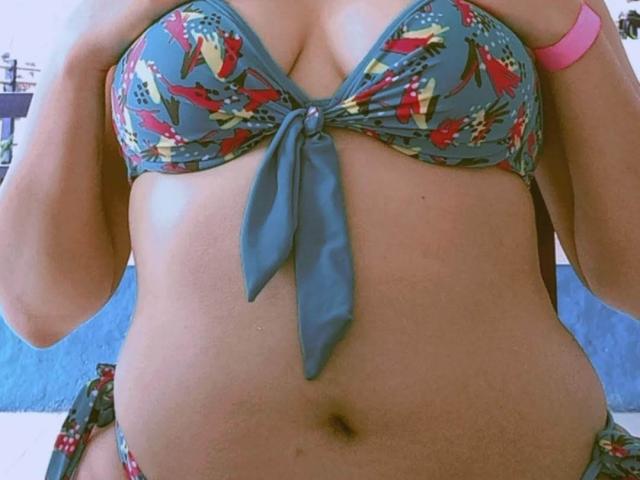 VictoriaF69 portant un bikini bleu à motifs floraux avec un nœud, montrant ses seins et son ventre, et portant un bracelet rose, sur une photo..