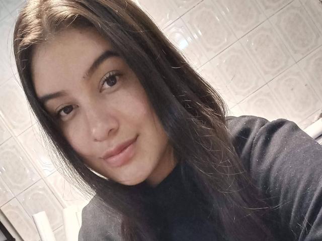 VictoriaF69 has long dark brown hair, brown eyes, and a slight smile, wearing a black turtleneck, with a soft, slightly chubby face and fair skin.