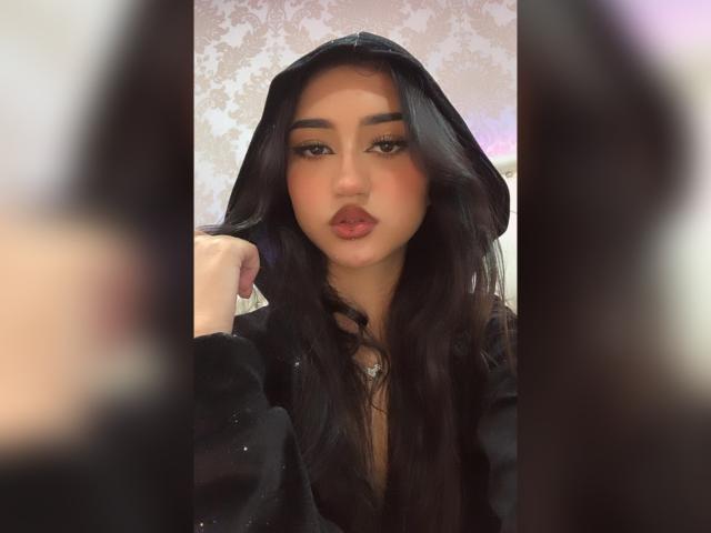 LuciaCalixto tiene el cabello oscuro y ondulado, ojos marrones y labios carnosos con lápiz labial rosa. Lleva una sudadera negra con capucha, y una mano toca su cabello. Bordes suaves y difuminados..