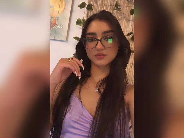 Lucia Calixto, con i suoi lunghi capelli neri, gli occhiali e la maglia viola, mostra le sue unghie curate, ha un carino piercing al naso e un leggero sorriso, con una luce soffusa sul viso..