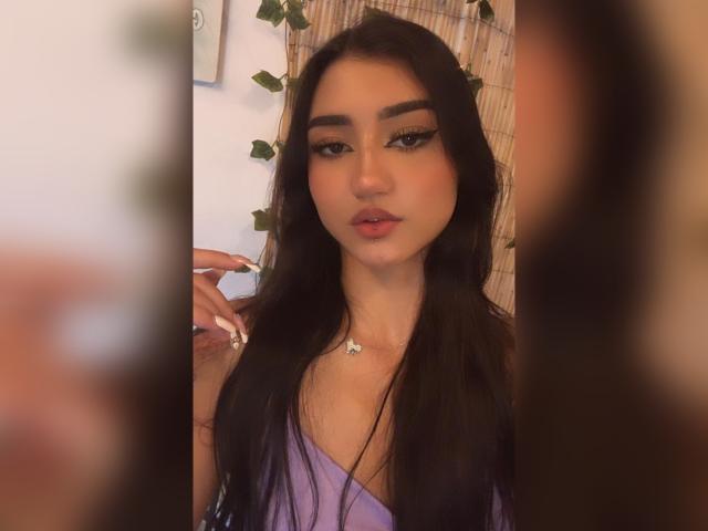 LuciaCalixto has long black hair, full eyebrows, and wears a purple top with a star necklace. Her lips are slightly parted, and she has a confident, sexy look.