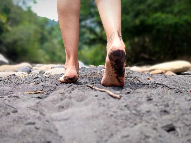 Le fessier nu et sale de KatrinaBello et son pied foulent du sable noir et granuleux, avec un tatouage visible sur sa cheville, et ses orteils sont légèrement recourbés..