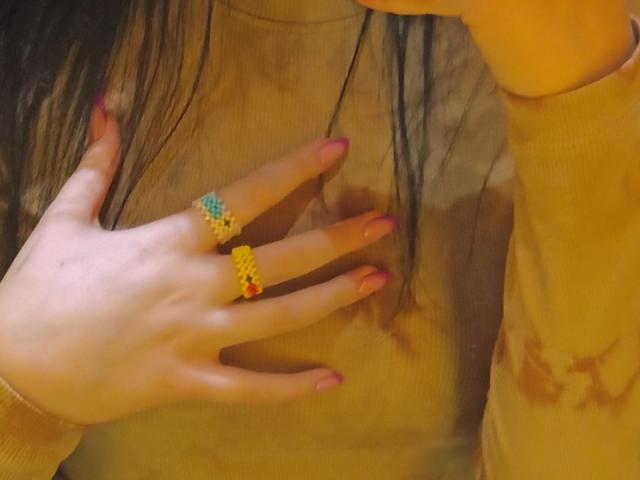 La main de Zanoza, avec ses ongles roses, une bague jaune sur l'annulaire et une bague jaune sur l'index, effleure sa chemise marron avec une tache jaune..