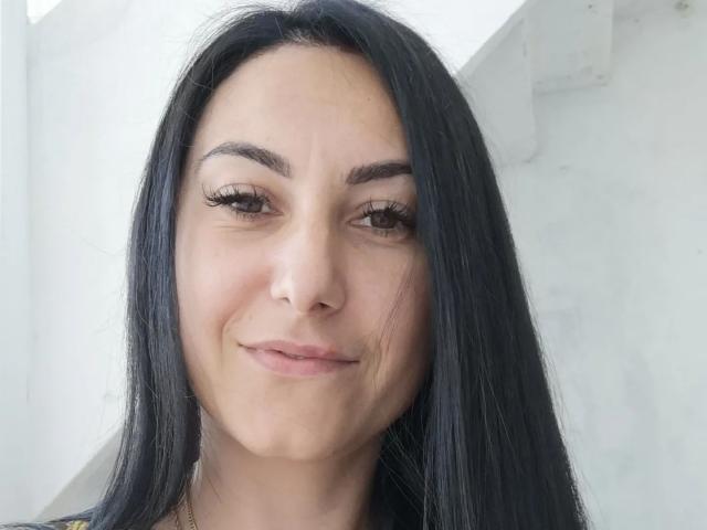EvilFindom tiene el pelo largo y negro, ojos marrones y una ligera sonrisa con un maquillaje sutil, que muestra una piel clara y un rostro lindo. Sus pestañas son largas y lleva una blusa negra..