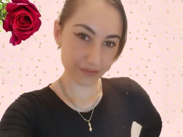 EvilFindom tiene la piel clara, ojos marrones y cabello negro recogido en una coleta. Lleva una blusa negra, un collar de plata y un pequeño colgante con forma de cruz. Una rosa roja está en la esquina superior izquierda..