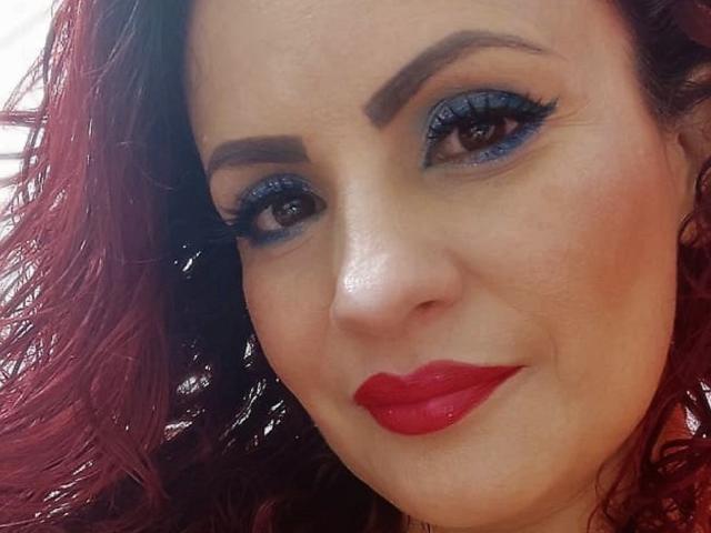 Karina Molina ha il rossetto rosso, l'ombretto blu e i capelli rossi ondulati, con un sorriso compiaciuto sul viso, che mette in risalto le sue sopracciglia scure e le lunghe ciglia..