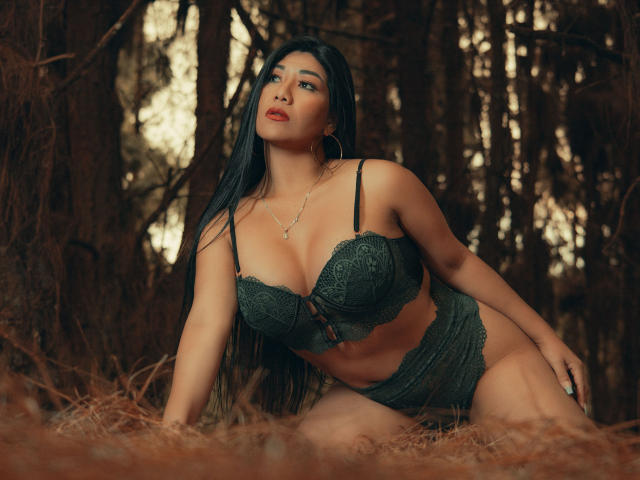 KhloeLawson with long black hair, green lace bra and panties, medium tits, curvy ass, kneeling in forest, looking up, red lipstick, hoop earrings, necklace, sexy, attractive.