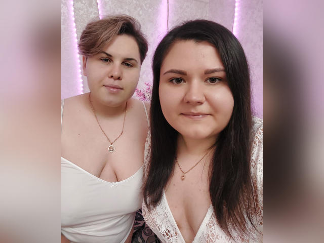 Becky e Ellen, con piccoli seni, indossano top bianchi, mostrando il décolleté, in un selfie. Becky ha i capelli corti e castano, mentre Ellen ha i capelli lunghi e scuri. Entrambe hanno un sorriso dolce..
