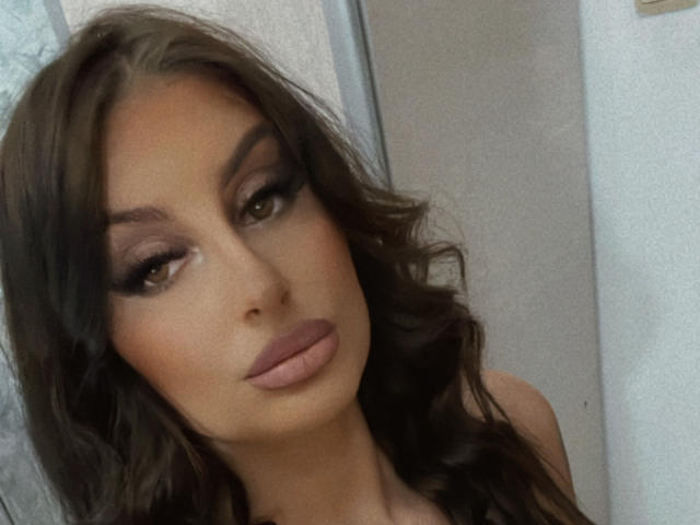 CassieSin hat braunes, welliges Haar, Smokey-Eye-Make-up und volle, rosafarbene Lippen. Ihre sinnlichen, braunen Augen sind halb geöffnet, was ihr einen verführerischen Ausdruck verleiht. Ihre gebräunte Haut ist makellos..
