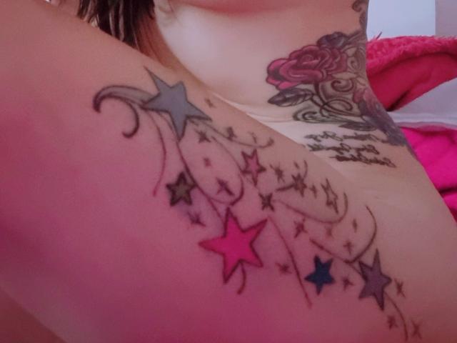 LindaSmith's tits have a colorful tattoo of stars and swirls on her chest, with pink and blue stars, and a rose tattoo above her right breast.