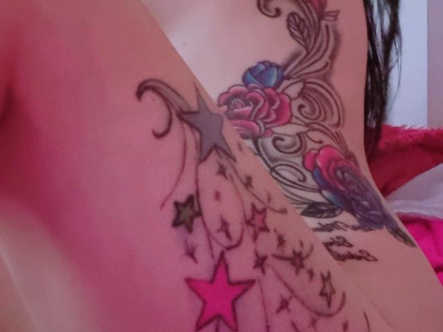 LindaSmith's side tattoo features colorful roses, stars, and swirls in black, pink, and blue. Her bare back and pink star prominently stand out.