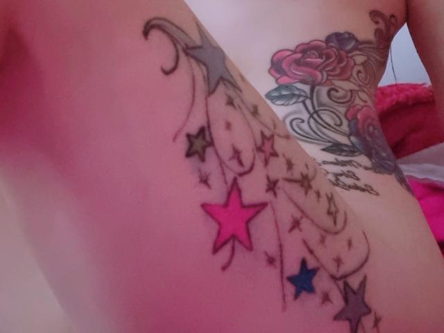 LindaSmith's side tattoo featuring pink, blue, and black stars with curly lines, and a colorful rose on her ribcage. Her pale skin is visible.