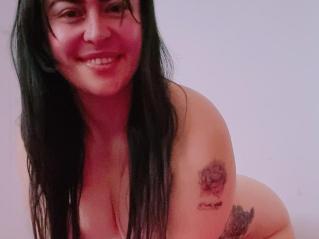 LindaSmith is a naked woman with long black hair, smiling at the camera, showing tattoos on her right shoulder and upper arm, with her tits visible.