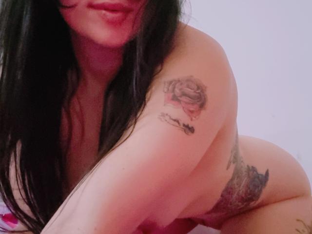 LindaSmith is nude, kneeling, with long black hair, showing tattoos on her right arm and hip. Her ass is partially visible. Her tits are not in the frame.