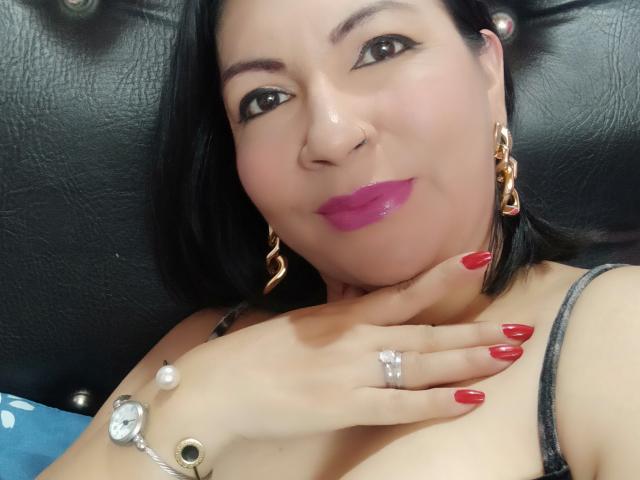 Amanda Kohler heeft roze lippenstift, rode nagels, een neusring en gouden oorbellen. Ze raakt haar nek aan met een hand met een ring, en draagt een zwarte bandeau..