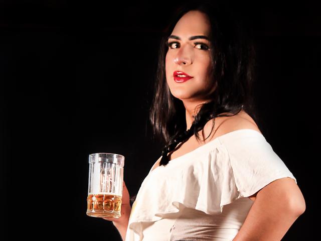 IrisDurand with dark hair in a braid, red lipstick, white off-shoulder top, holding a glass of whiskey, black background, looking to the side, slightly smug.