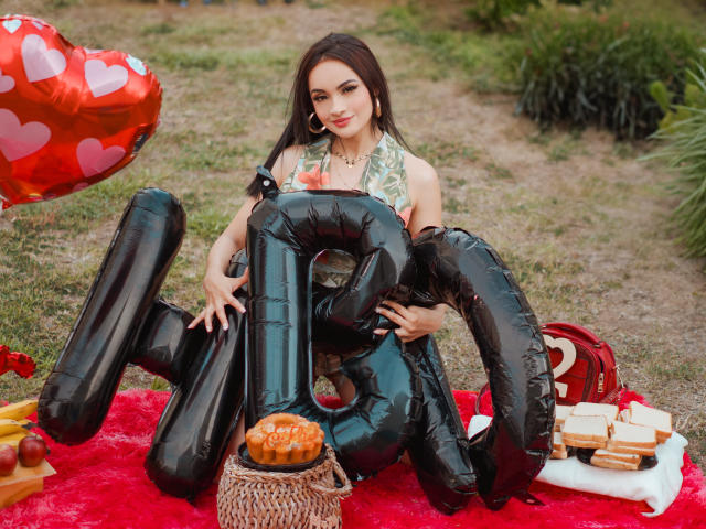 AngelCutie mit einer schwarzen, aufblasbaren Zahl '10', trägt ein grünes Halstuch-Top, sitzt auf einer roten Decke, hält einen Korb mit Brot, mit einem Herz-Ballon und einem Picknick..