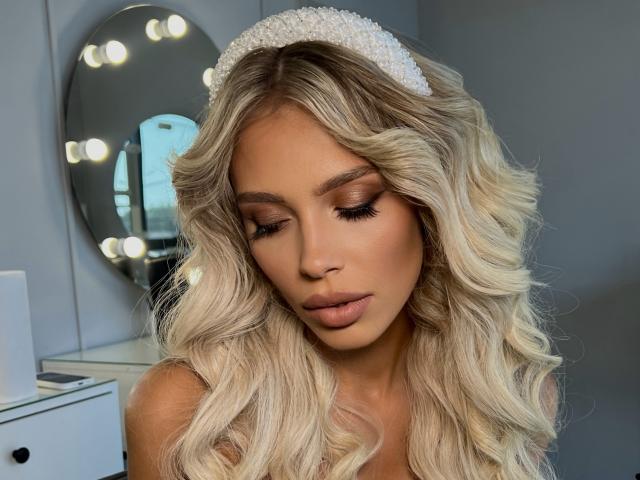KateLilly with blonde, wavy hair, wearing a white headband, has her eyes closed, showing off her full, glossy lips and makeup. Her tits are partially visible.