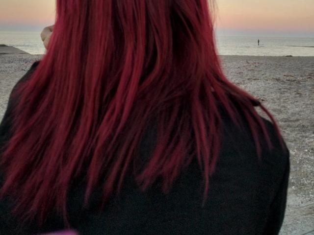 Les cheveux roux, légèrement en désordre et de longueur moyenne de Zanoza sont visibles sur le devant, elle porte un haut noir, et on aperçoit une petite main tatouée de blanc en arrière-plan, près d'une plage au coucher du soleil..