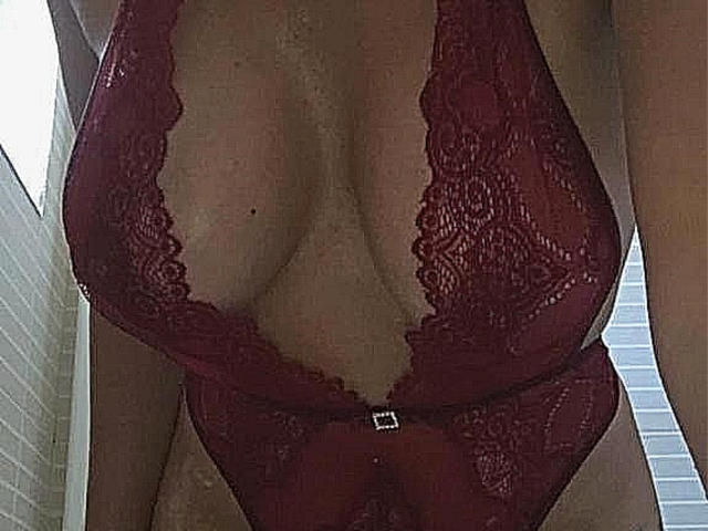 InanAIshtars wearing a deep red lace bodysuit with a plunging neckline, showing her big, bare tits and cleavage. The lace is intricate and she's standing.