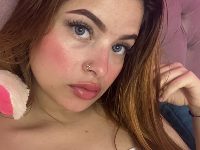 ShantalSummer ha un incarnato rosato, labbra piene, occhi azzurri e un piercing al naso. I suoi capelli castani sono sciolti e tiene in mano una spalla imbottita rosa e bianca..