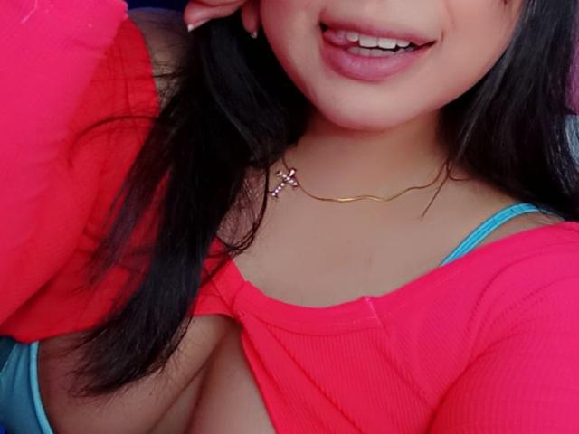 AlizeeTorres with medium tits in a red top, blue bra showing, gold necklace, black hair, tongue out, smiling, pink lips, and a cute, sexy look.