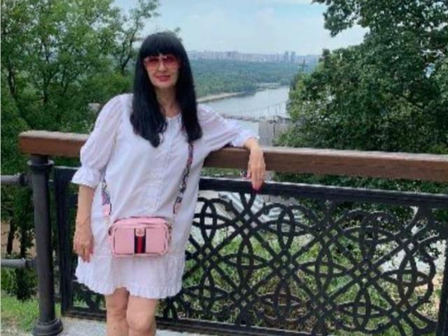 MelanyBanks has black hair, red sunglasses, and a white dress with lace. She's leaning on a wooden railing with a pink purse, standing outdoors, showing her ass.