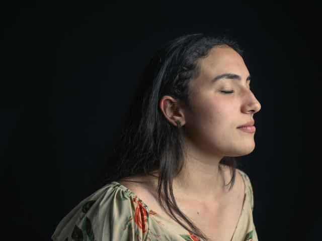 HelaViKy ha gli occhi chiusi, i capelli scuri e un sorriso appena accennato. Indossa un abito floreale, con il naso leggermente all'insù, su uno sfondo nero..