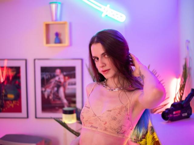 Yorogumo with long brown hair, pale skin, and small tits wearing a pink patterned bra, necklace, and blue highlights, standing in a neon-lit room, touching her hair.