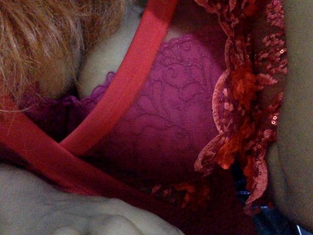 Jazzlyn's red lace bra with floral patterns, showing her boobs, has a red strap and orange floral lace trim, with her light brown hair partially visible.