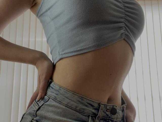 SugarrX's ribbed blue crop top shows her small boobs and flat stomach. She's wearing faded jeans with her hands on her hips, showing a bit of her ass.
