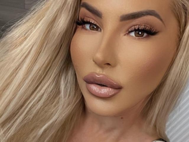 MelisaLauren's face, featuring blonde hair, brown eyes, full pink lips, and thick eyebrows, with a sexy, sultry expression. Her makeup is flawless, highlighting her attractive features.