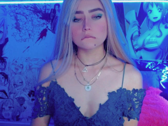 Sabrina Olsons, con i suoi lunghi capelli blu, gli occhi azzurri e una piccola lentiggine sul labbro superiore, indossa una blusa di pizzo con una spalla scoperta, che mette in mostra il seno, ed è adornata da diverse collane..