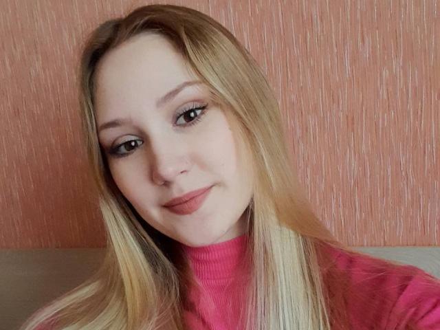 LaylaHott ha i capelli biondi, la pelle chiara e indossa un maglione a collo alto rosa. Sorride, ha un piccolo piercing al naso e un trucco leggero, e nella foto mostra il seno..