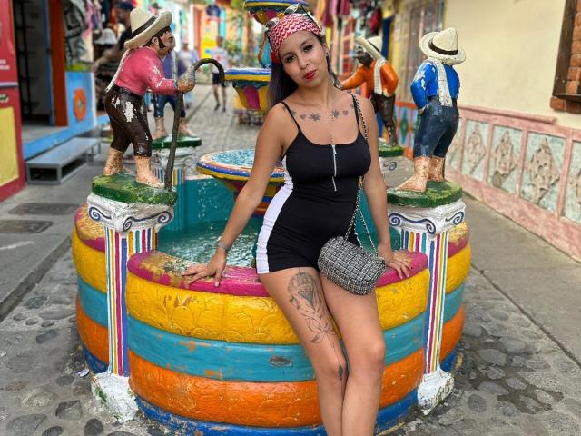 Samantha Morgan, schwarzes Tanktop und Shorts, große Brüste, tätowiertes Bein, schwarz-weiß gestreift, farbenfrohe Springbrunnen, rosa Kopftuch, graue Handtasche, stehend, farbenfroße Straße, Statuen..