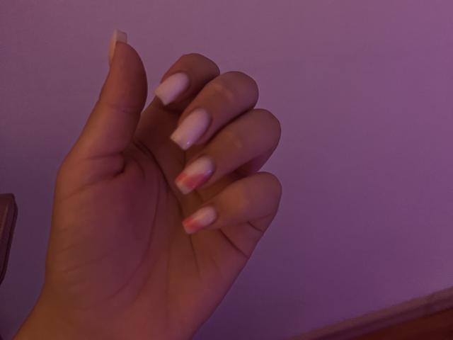 Destinis' hand with long, white and pink-tipped nails, palm facing up, under purple lighting. Her skin is light and her fingers are slightly curled.
