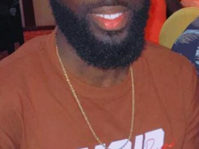 RebellKing's dark, curly beard and shiny red lips are visible. He's wearing a brown shirt and a gold chain, with his upper body in the frame.