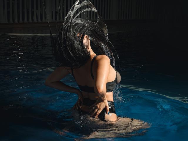 KamileNilsen, bikini negro y ajustado, de espaldas a la cámara, agua salpicando, manos en las nalgas, cabello oscuro ondeando, piscina azul, fondo sombrío, cuerpo tonificado, gotas de agua, sexy..
