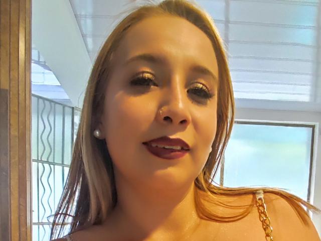 O rosto de Evelyn Swanth, com cabelos castanhos longos, brincos de pérola e batom vermelho, sorrindo levemente. Ela tem uma pequena perfuração no nariz e está usando uma pulseira laranja..