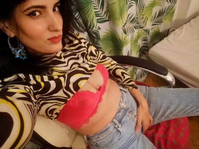 AddictedToUTS with dark hair, wearing a zebra-patterned top, pink lace bra, showing her tits, and blue jeans, sitting on a chair, looking at the camera.
